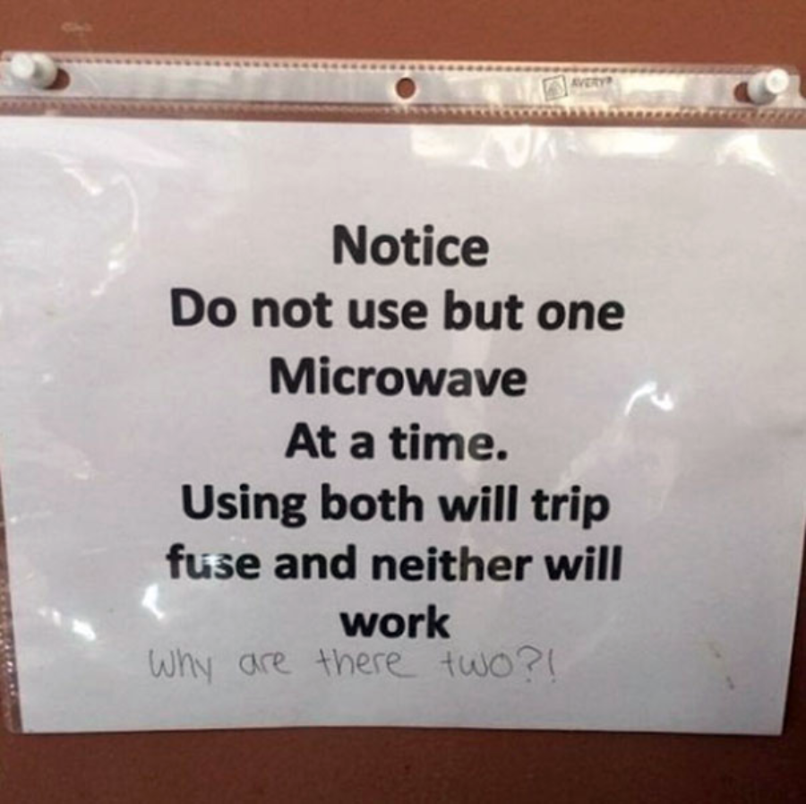 A printed sign says: "Notice Do not use but one Microwave At a time. Using both will trip fuse and neither will work." Below, handwritten text reads: "Why are there two?!