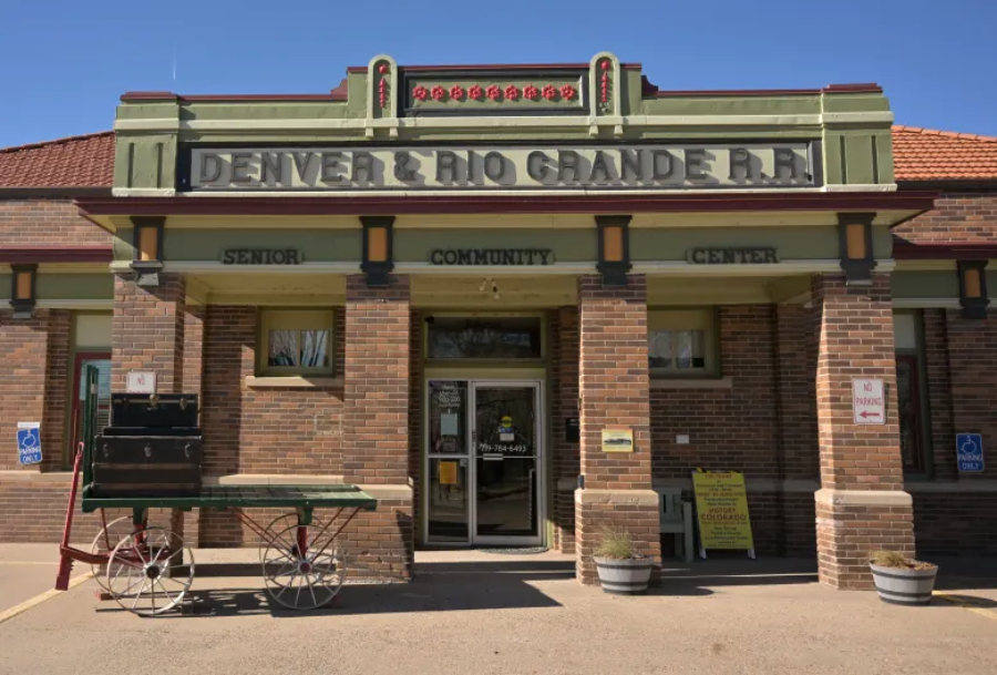 A historic brick building with a sign reading "Denver & Rio Grande R.R." above the entrance, labeled as a senior community center. A vintage wagon is parked in front, and handicapped parking signs are visible.