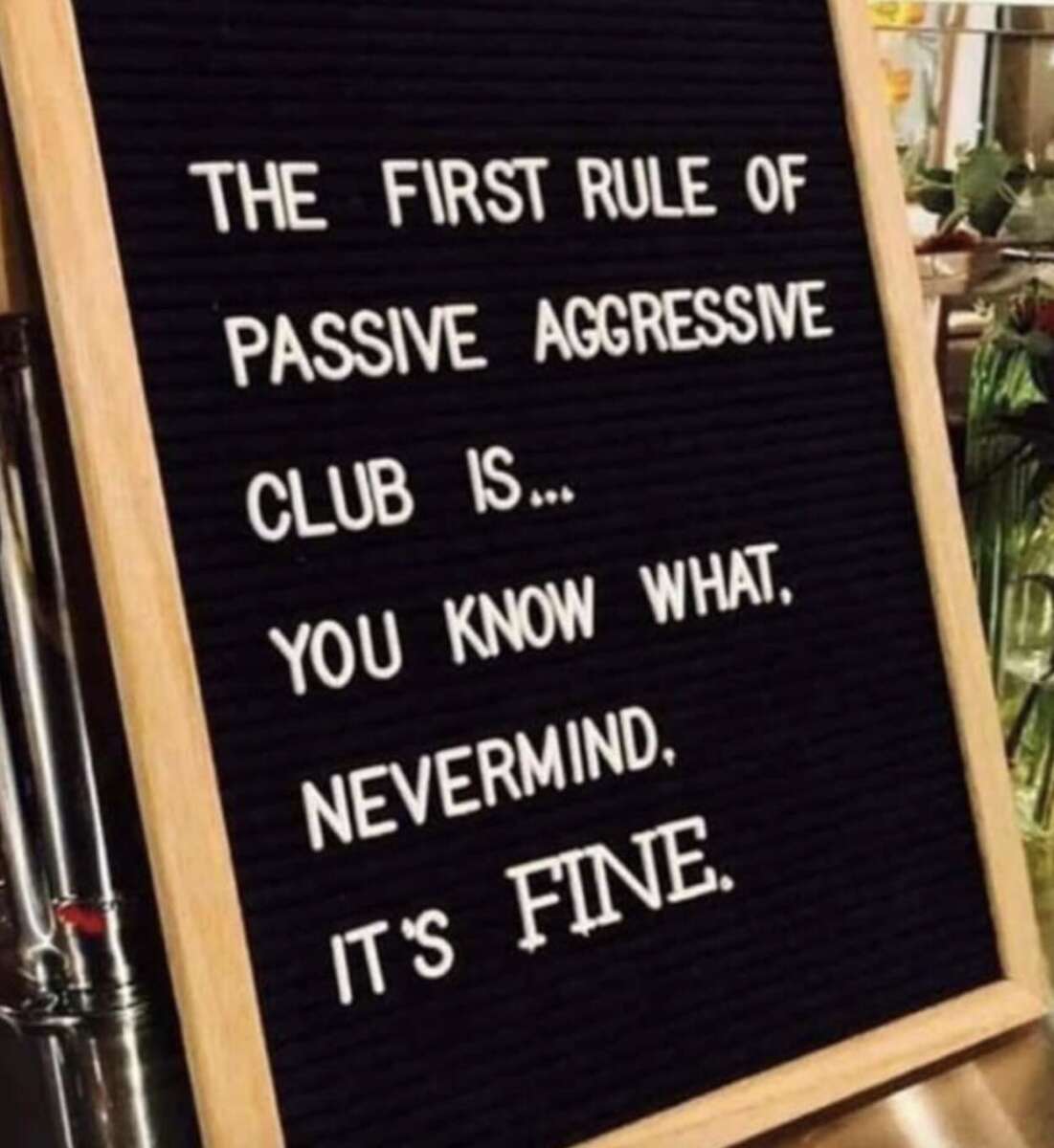 A black felt letter board with white letters reads: "THE FIRST RULE OF PASSIVE AGGRESSIVE CLUB IS... YOU KNOW WHAT, NEVERMIND. IT'S FINE." The board is framed in wood.