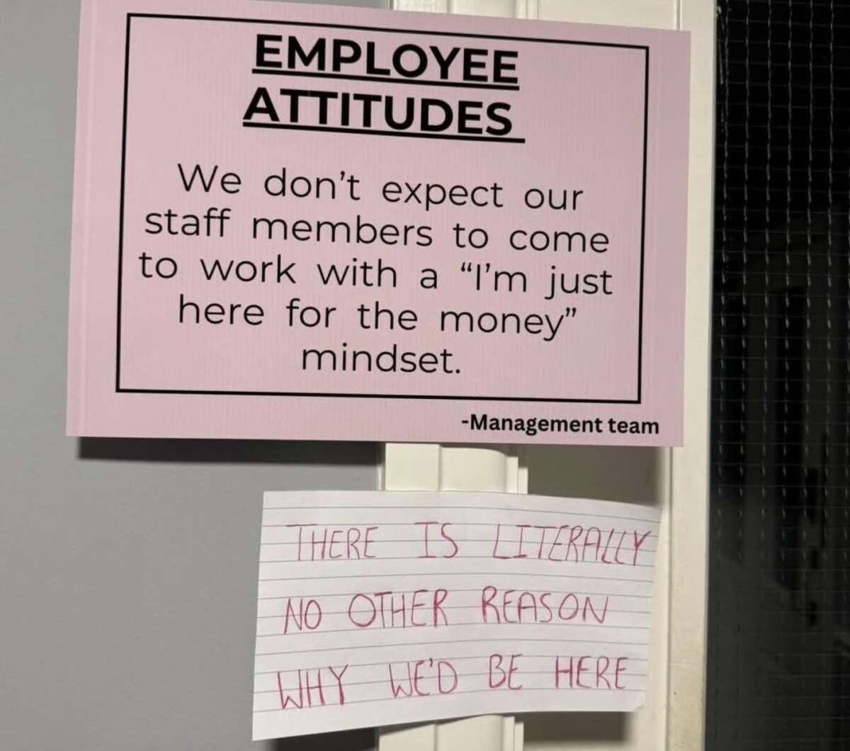 A printed sign reads, "EMPLOYEE ATTITUDES: We don’t expect our staff members to come to work with a ‘I’m just here for the money’ mindset." Underneath, a handwritten note says, "THERE IS LITERALLY NO OTHER REASON WHY WE’D BE HERE.