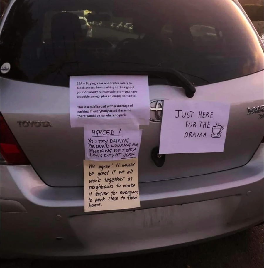 A silver Toyota car with three notes taped to the trunk, discussing parking issues. One says “Just here for the drama,” another is a typed explanation, and the third is a handwritten response suggesting neighbor cooperation.