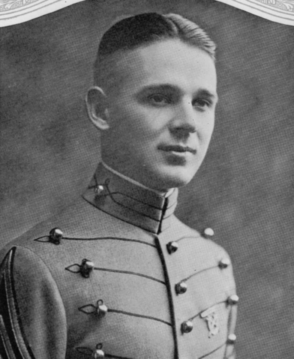 A young man in a formal military cadet uniform poses for a portrait. He has short, neatly combed hair and is looking slightly to the side. The photo is black and white with a neutral background.