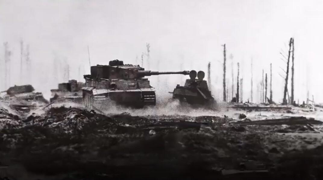 Two tanks drive through a muddy, desolate battlefield with bare, leafless trees and smoke or fog in the background, creating a somber and war-torn atmosphere.