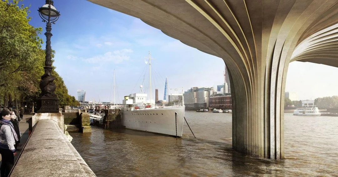 Two people stand by a riverside walkway with ornate lamp posts and trees, overlooking a docked white ship and the river. An architectural structure with sweeping arches rises from the water on the right. City buildings are visible in the distance.
