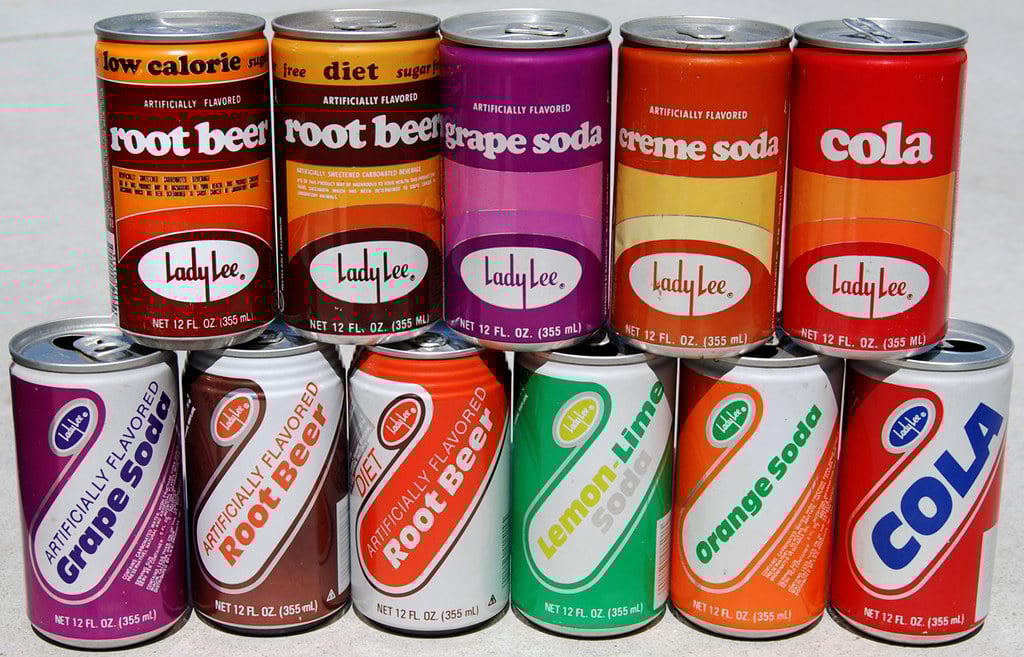 Ten colorful vintage Lady Lee soda cans in two rows, featuring flavors like root beer, grape, creme, cola, lemon-lime, and orange. Each can has distinct retro-style labels and bold colors.