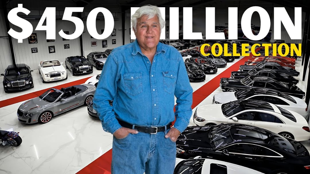 A man in a blue denim shirt stands in front of a large luxury car collection inside a showroom. Bold text above reads “$450 MILLION COLLECTION.” Dozens of cars are arranged in neat rows on white and red flooring.