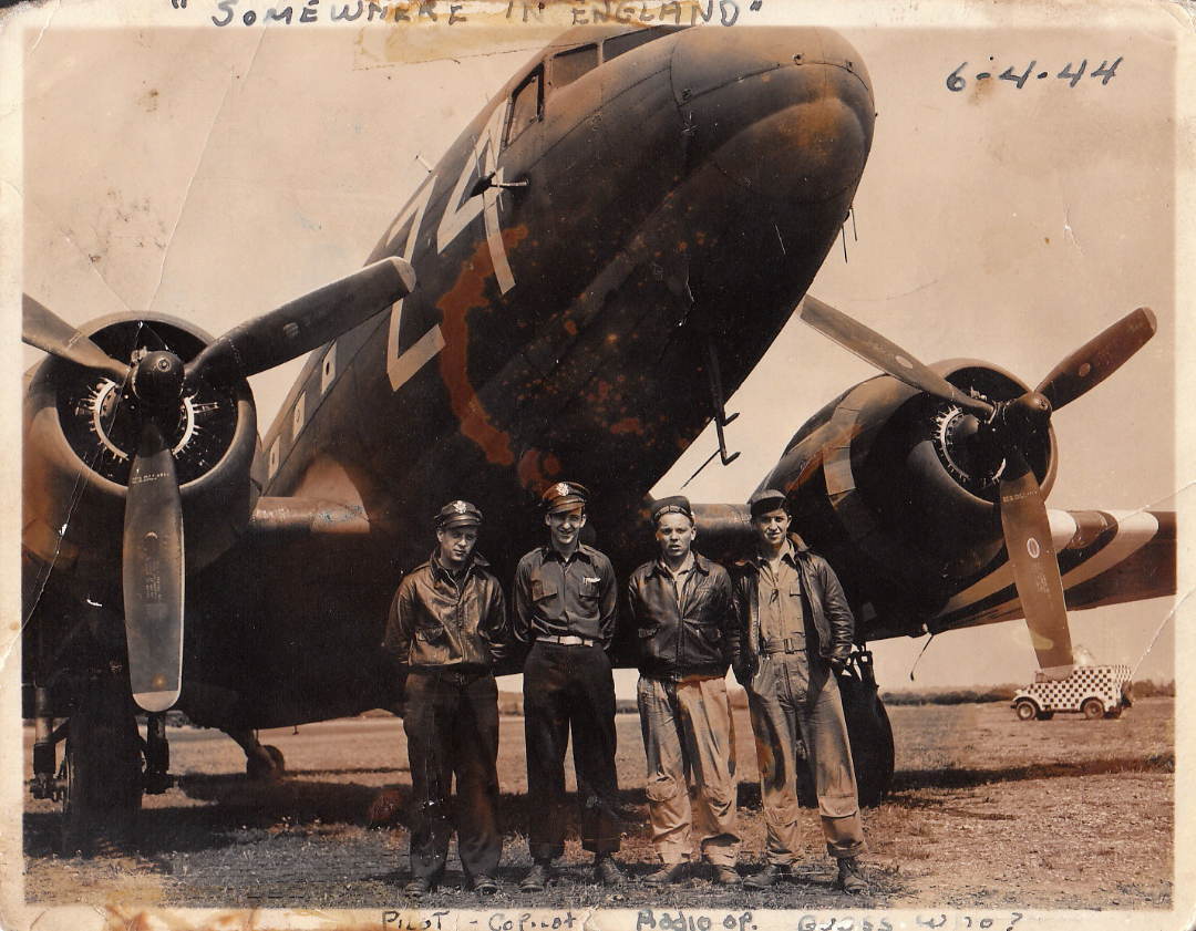 Four World War II-era airmen stand in front of a large military aircraft on a grassy airfield. The photo is sepia-toned, with handwritten notes reading "Somewhere in England" and dated 6-4-44 along the top.