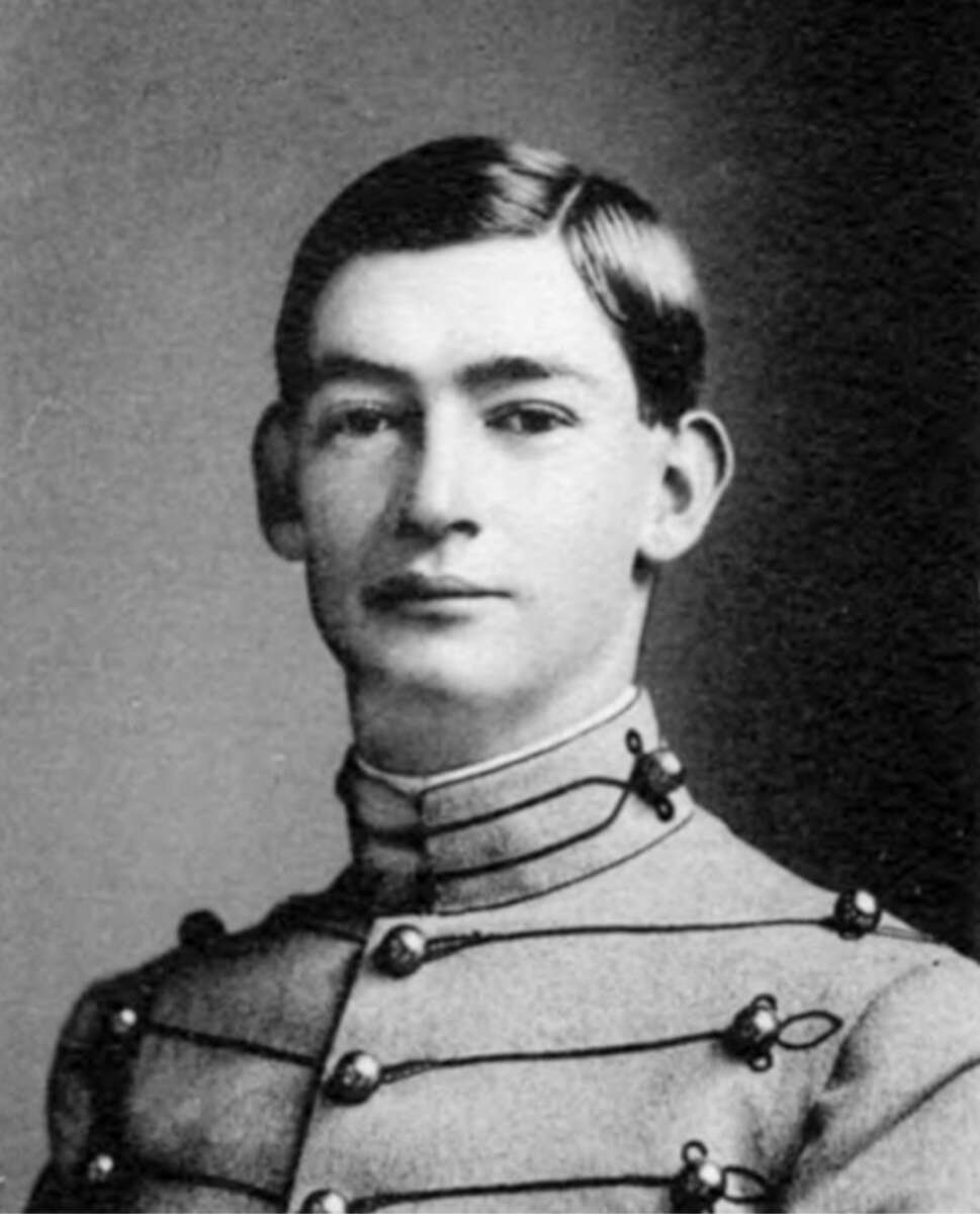 A young man with short, dark hair poses for a formal portrait, wearing a high-collared military uniform with decorative buttons and braiding. The image is in black and white.