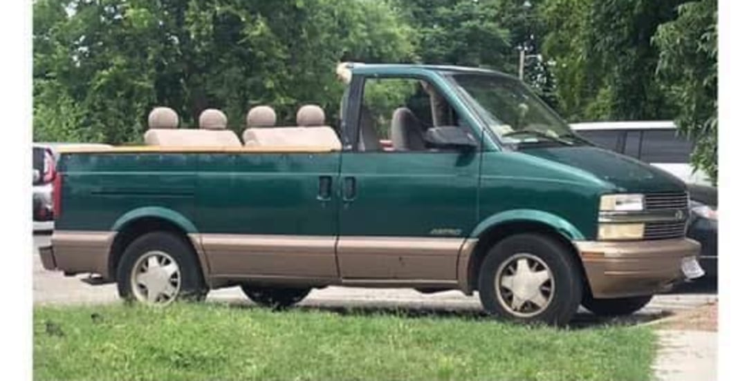 A green and tan van with its roof and windows removed, creating a convertible look. The van has four visible seats and is parked outdoors near trees and other cars.