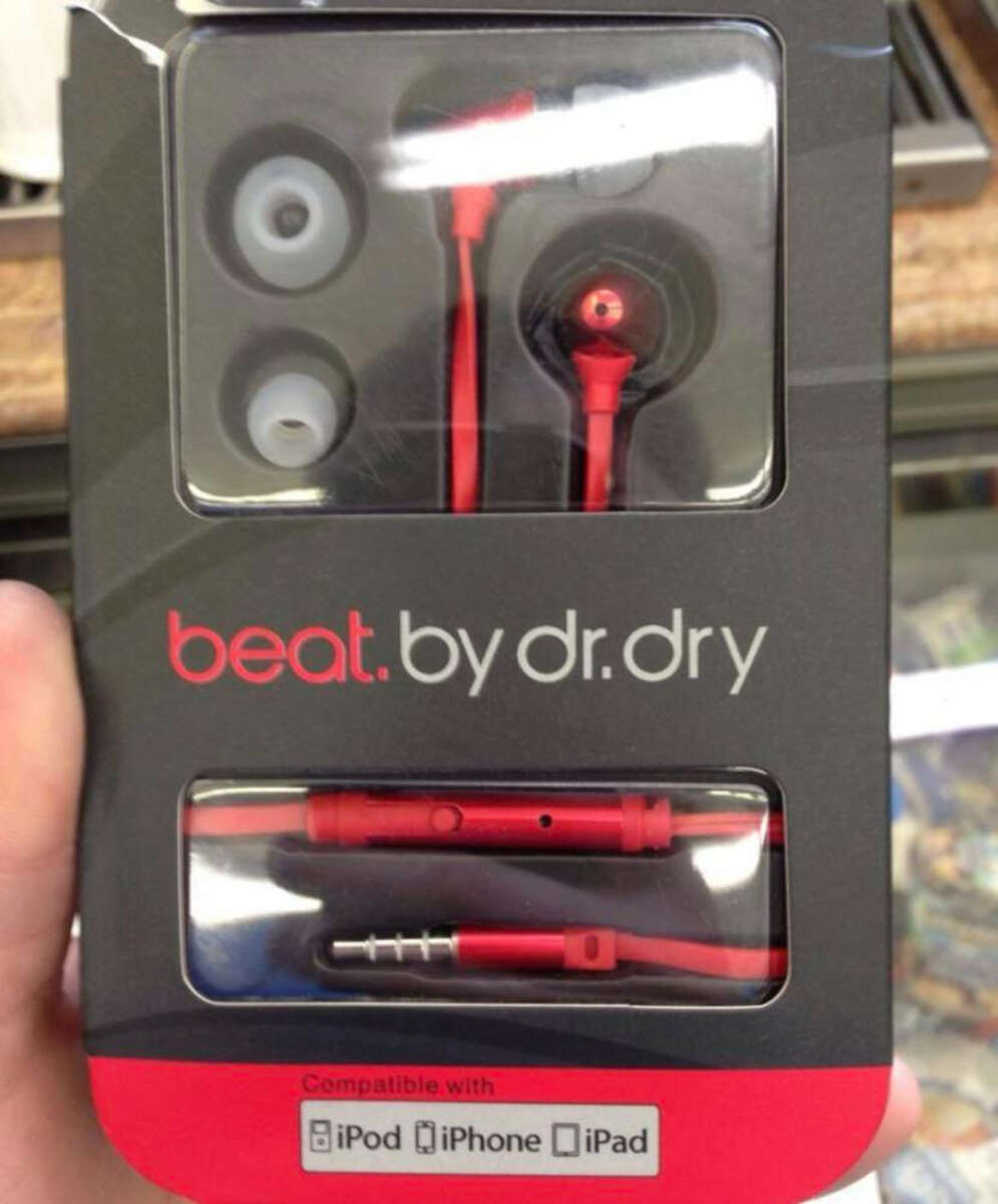 A hand holds a box of red earbuds labeled "beat.by dr.dry," resembling Beats by Dr. Dre branding. The packaging shows extra ear tips and notes compatibility with iPod, iPhone, and iPad.