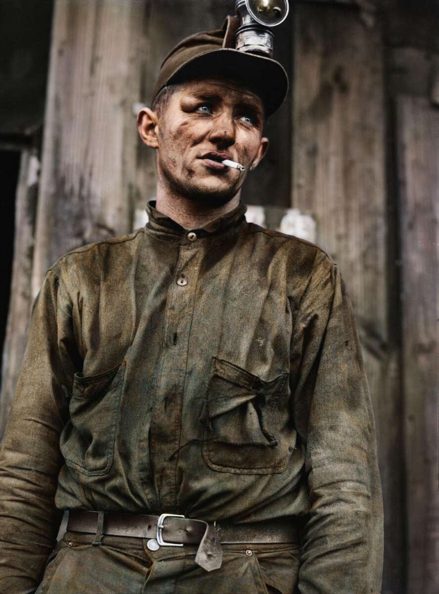 A coal miner wearing a dirt-stained uniform and helmet with a headlamp stands in front of wooden boards, looking to the side with a cigarette in his mouth. His face and clothes are marked with grime.