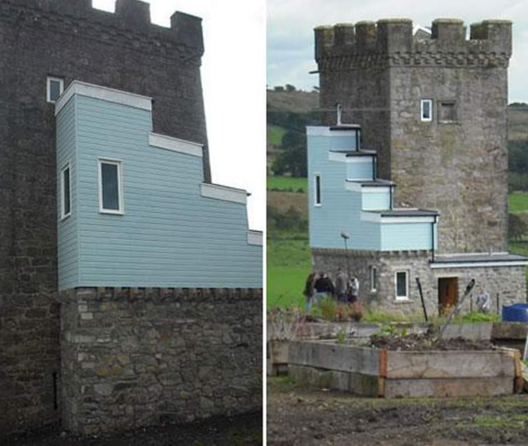 A stone castle tower with a modern, light blue, stepped extension attached to one side. The extension has rectangular windows and contrasts sharply with the historic architecture.