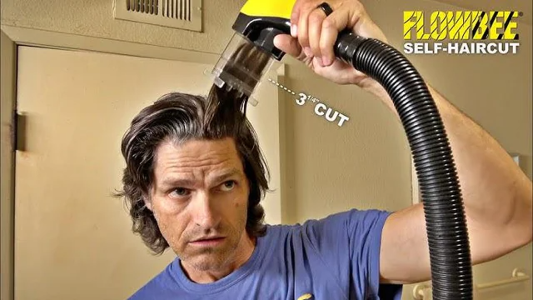 A man uses a Flowbee vacuum haircutting device to trim his hair in a bathroom, aiming for a 3 1/2 inch cut; the Flowbee logo and "SELF-HAIRCUT" text appear in the top right corner.