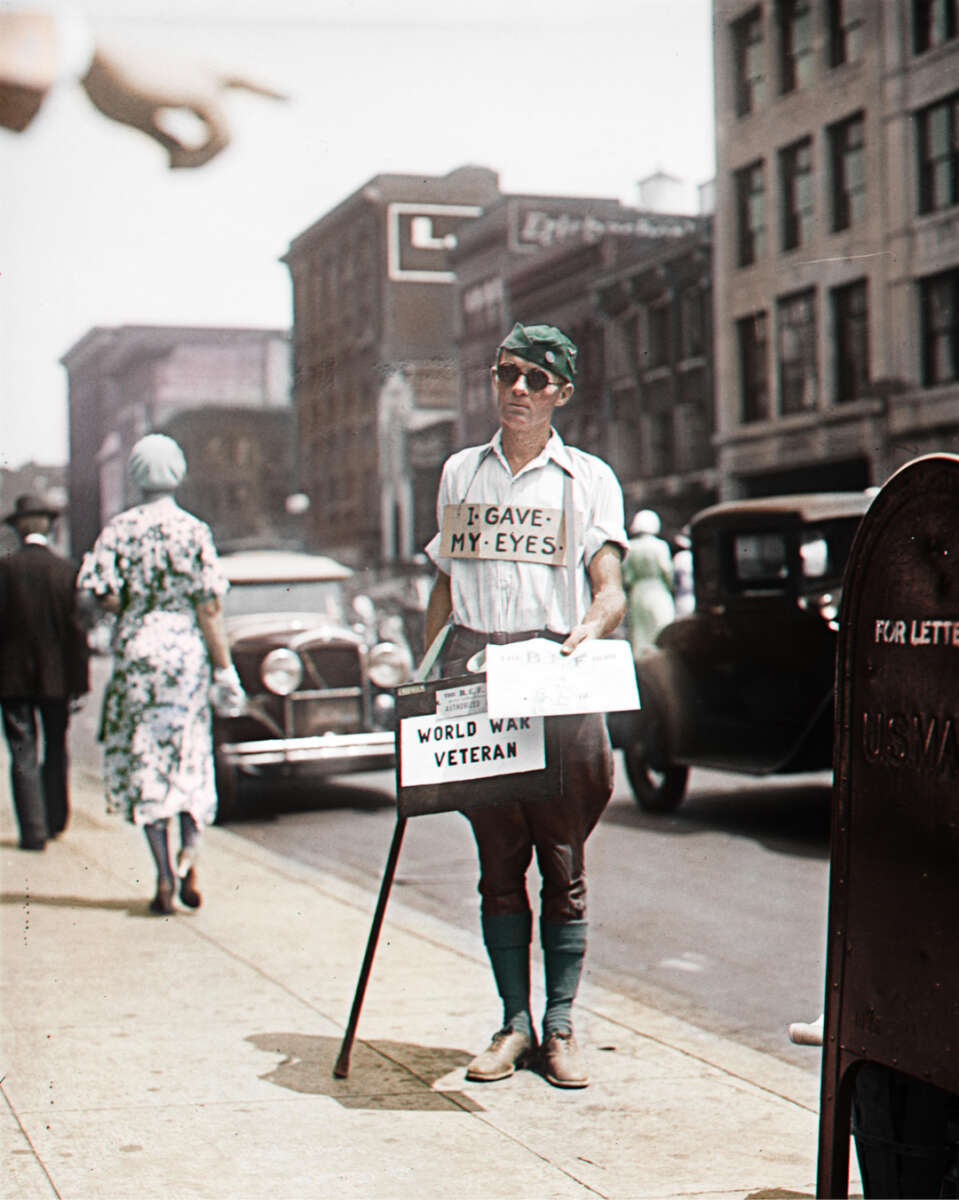 A man with dark glasses, a headscarf, and a sign reading "I Gave My Eyes – World War Veteran" stands on a city sidewalk holding a donation box. Vintage cars and pedestrians are in the background.