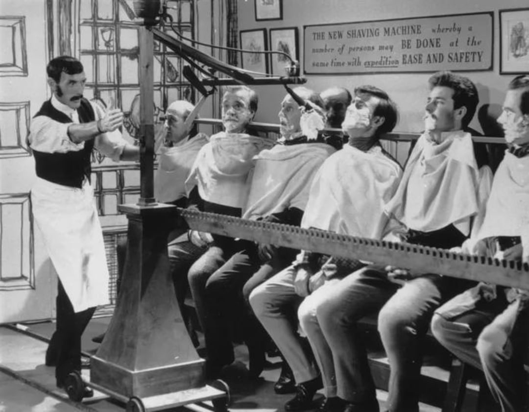 A vintage black-and-white photo shows seven men seated in a row with barber capes, facing a large mechanical device labeled "The New Shaving Machine," while a barber prepares to operate it.