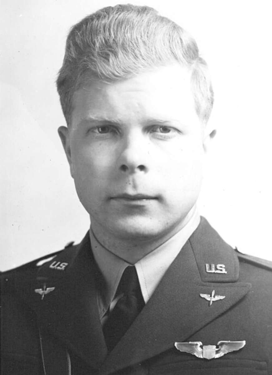 A black-and-white portrait of a U.S. military officer in uniform, wearing a tie and displaying aviation insignia on his lapels and chest. The man has light-colored hair and a serious expression, looking directly at the camera.