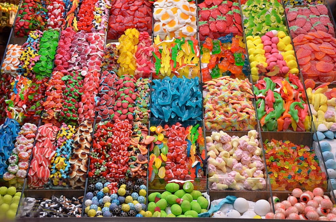 An overhead view of assorted colorful candies displayed in organized rows, including gummies, marshmallows, licorice, and sour candies in various shapes and vibrant colors.