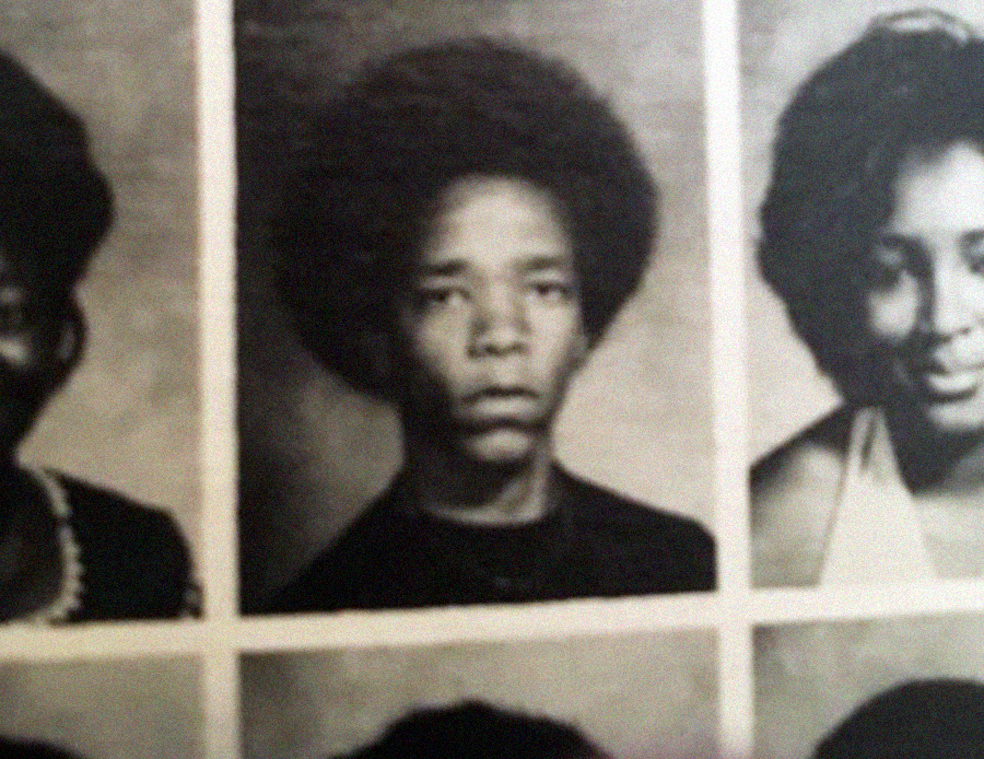 A black-and-white yearbook photo of a young person with a large afro hairstyle, wearing a dark shirt, looking directly at the camera with a neutral expression. Other yearbook photos are partially visible around the image.