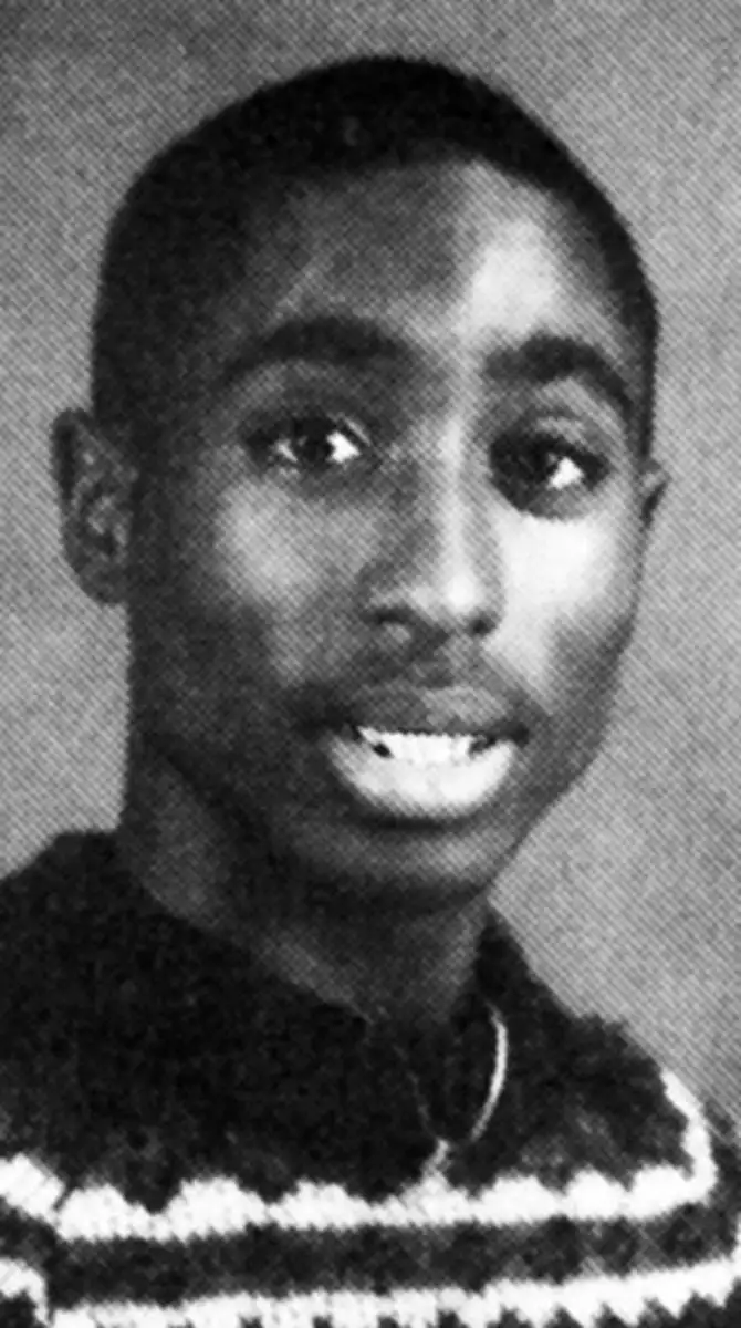 Black and white portrait of a young person with short hair, looking slightly to the side and wearing a striped sweater. The background is a plain, light tone.
