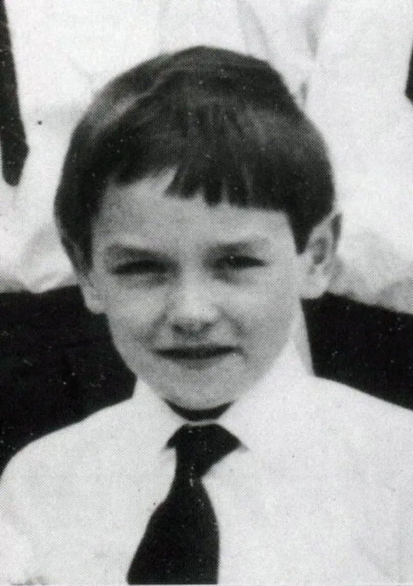 A young boy with short dark hair wearing a white shirt and a dark tie, looking at the camera and smiling slightly. The photo is in black and white.