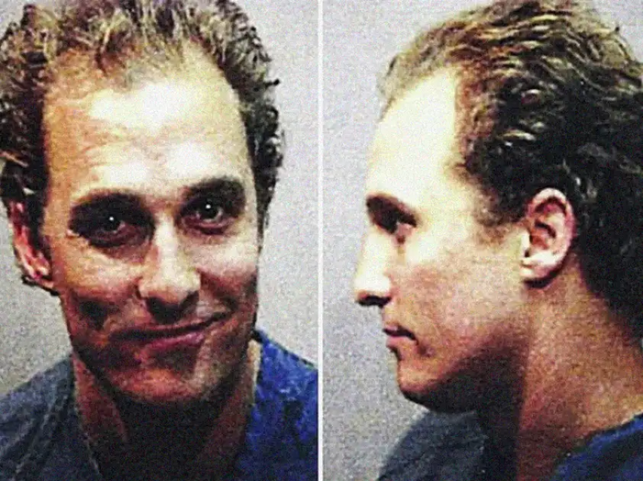 A man with curly hair wearing a blue shirt is shown in two mugshot-style photos, one facing forward and one in profile. He has a slight smile and a neutral expression.