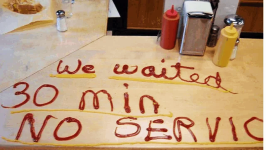 Ketchup and mustard on a counter spell out "We waited 30 min. NO SERVICE" near condiments and napkin holders, expressing frustration over not being served.
