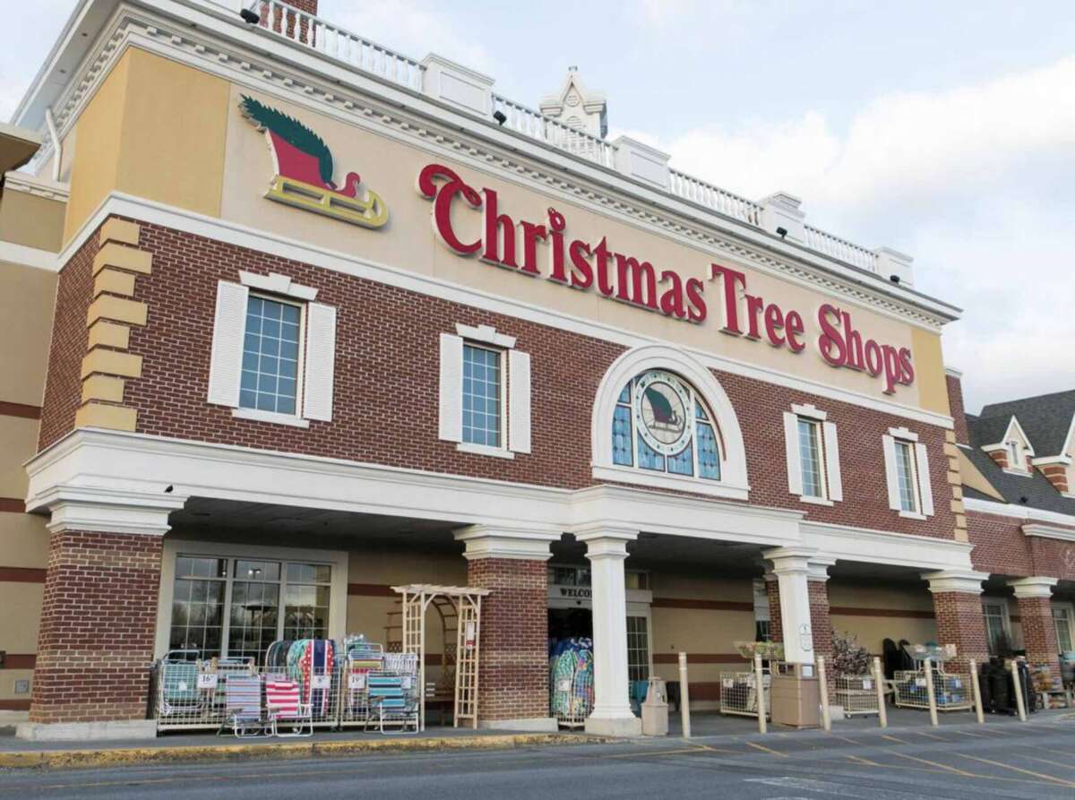The front of a Christmas Tree Shops store with a large red sign and a sleigh logo above the entrance, outdoor racks displaying various goods, and a mostly empty parking lot.