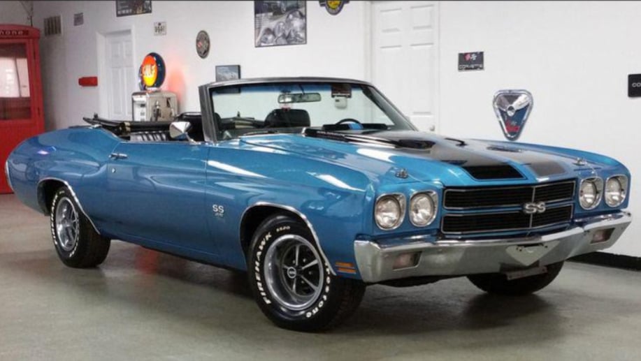 A blue 1970 Chevrolet Chevelle SS convertible with black racing stripes is parked indoors in a showroom with white walls and vintage car decor.