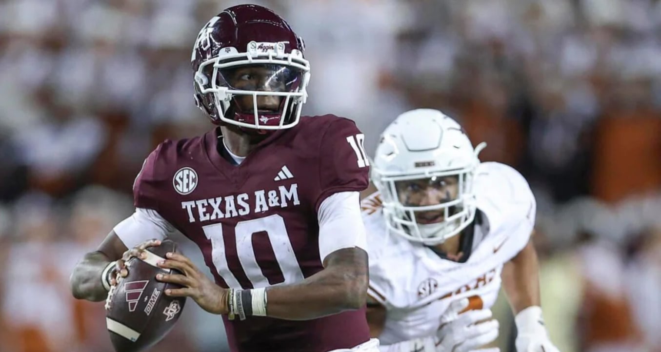 A Texas A&M football player in a maroon jersey prepares to throw a pass while being pursued by a defender in a white uniform during a game.