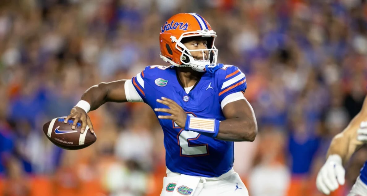 A college football player in a blue Florida Gators uniform and orange helmet prepares to throw a football during a game. The background is blurred with fans and players visible.