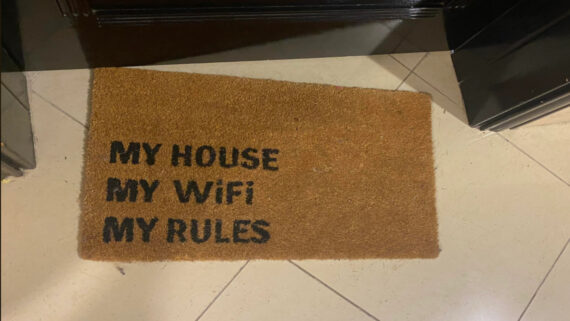 A brown doormat on a tiled floor with black text that reads: "MY HOUSE MY WiFi MY RULES.