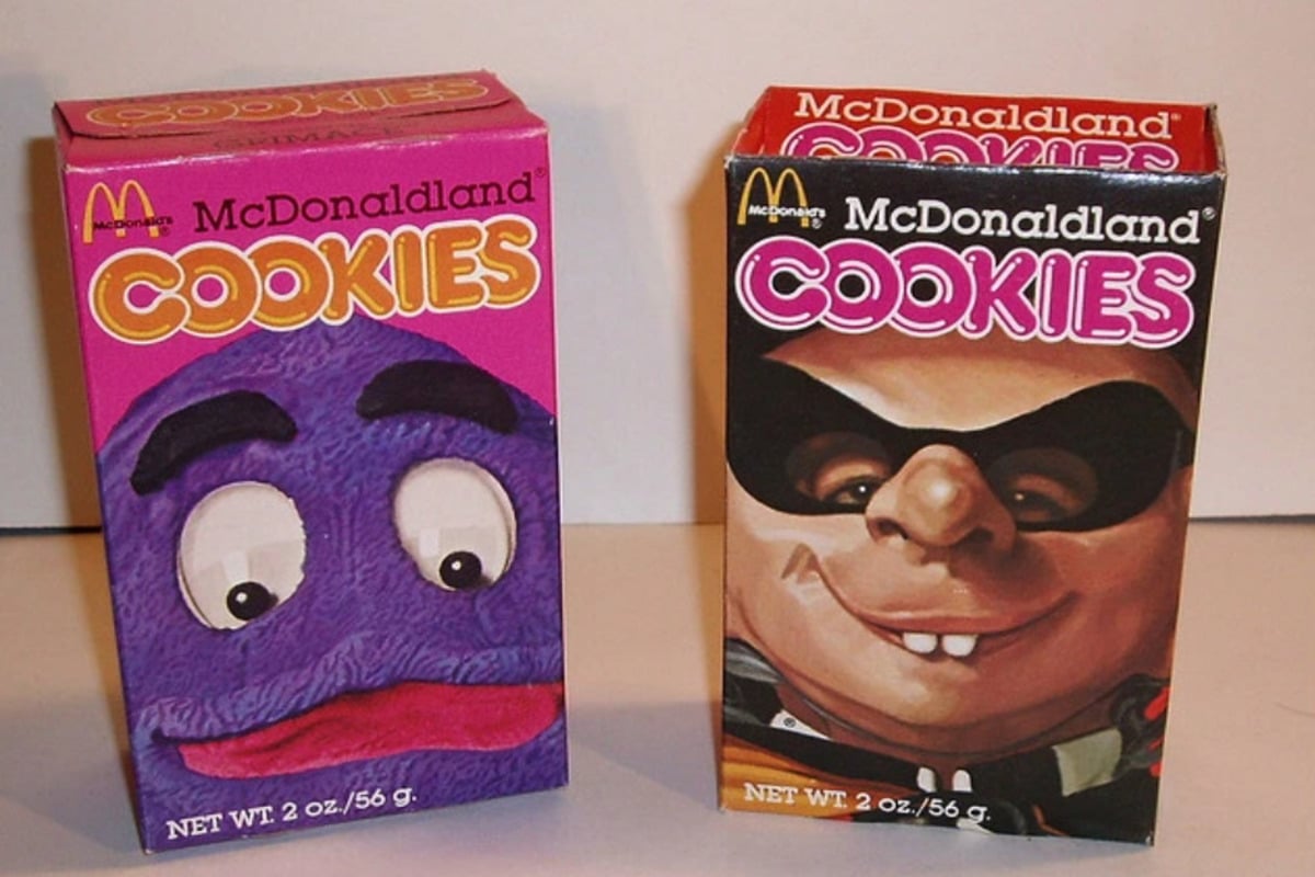 Two colorful vintage McDonaldland Cookies boxes are shown. The left box is purple with Grimace's face, and the right box is brown featuring the character Captain Crook. Both have bold “COOKIES” text and weigh 2 oz./56g.