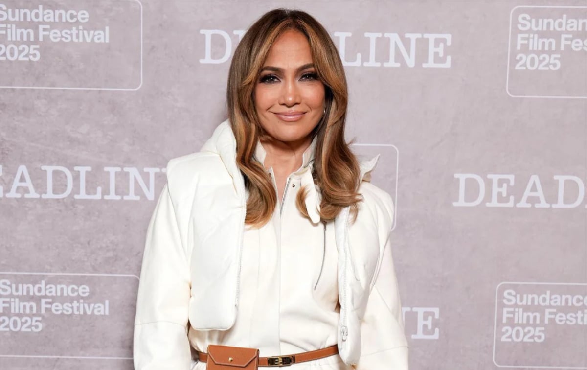 A woman in a white outfit with loose, wavy, light brown hair poses and smiles in front of a backdrop with "Sundance Film Festival 2025" and "DEADLINE" logos.