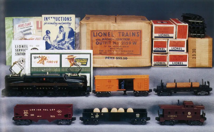 A vintage Lionel train set is displayed with a locomotive, cars, caboose, original boxes, instruction manuals, and Lionel Service Station pamphlets arranged neatly on a gray surface.