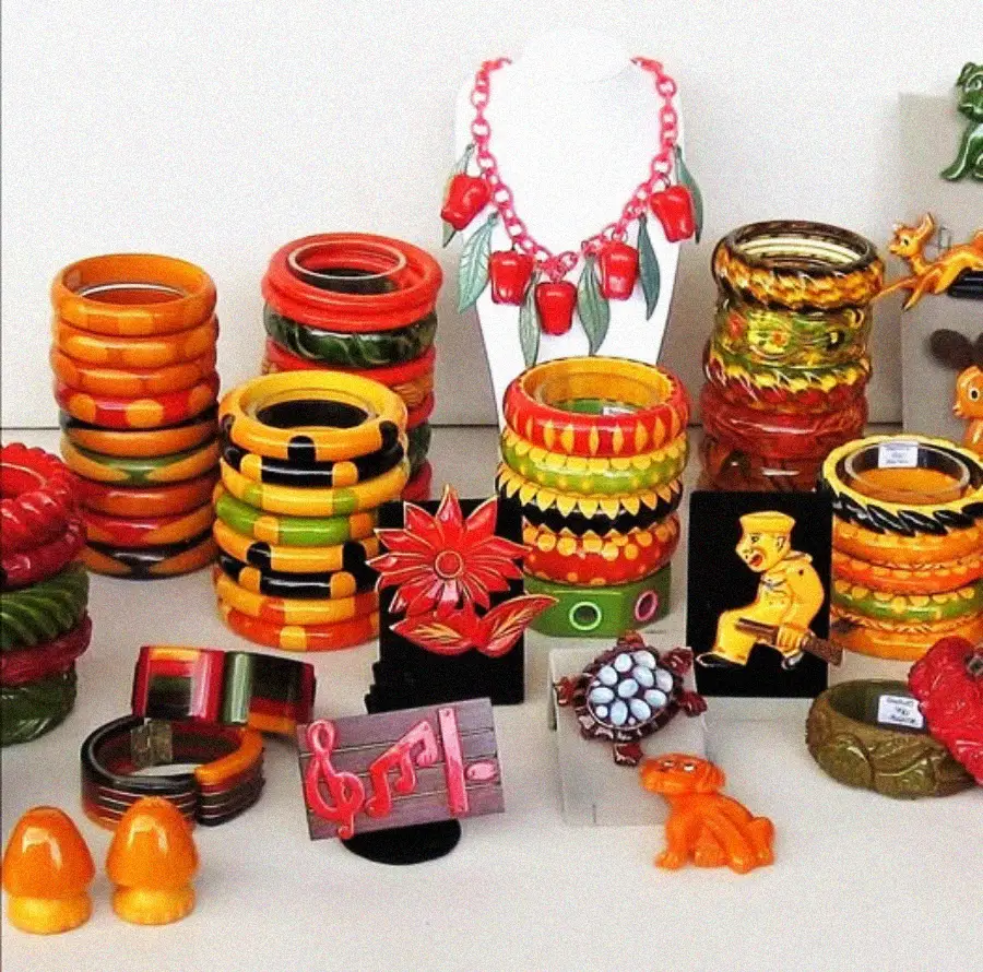 A colorful display of vintage plastic jewelry, featuring stacks of chunky bangles, bold necklaces, brooches shaped like animals and music notes, and earrings, all in bright, retro colors like orange, yellow, and green.
