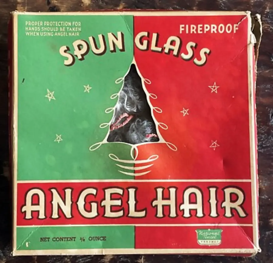 Vintage box labeled "Spun Glass Angel Hair," red and green with a triangular window showing white spun glass inside. Text notes it is fireproof and cautions “proper protection for hands should be taken.”