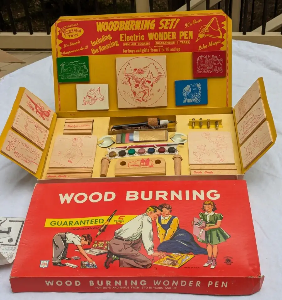 A vintage wood burning set with an open yellow box displaying tools, paints, instruction sheets, and a red lid featuring illustrations of children using the kit. The set includes an electric pen and various art supplies.