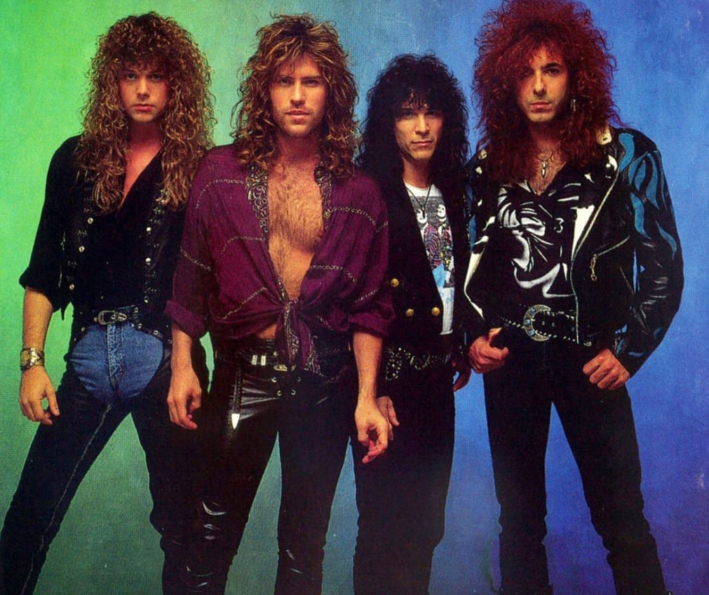 Four men with long, curly hair and dramatic 1980s rock fashion—leather pants, jackets, and deep V-neck shirts—stand against a blue and green gradient background, posing confidently for the camera.