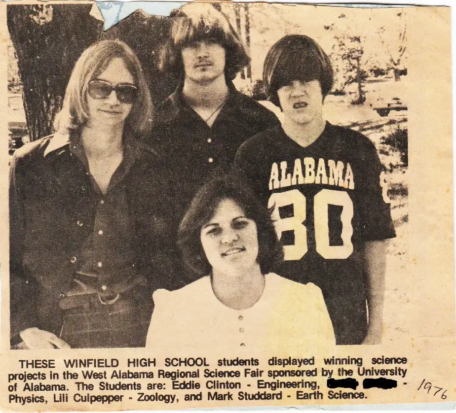 Four high school students, three standing and one sitting, pose outdoors. The standing students wear casual clothes, including an "Alabama 80" t-shirt. The caption below describes their science fair achievements.