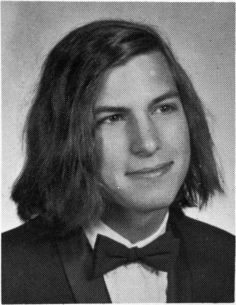 Black and white yearbook-style portrait of a young man with shoulder-length hair, wearing a tuxedo jacket, white shirt, and bow tie, looking slightly to the side with a faint smile.