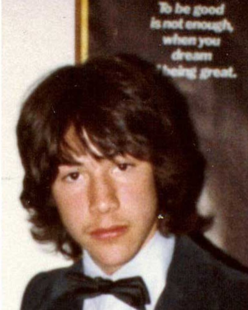A teenage boy with medium-length brown hair and a serious expression wears a suit and bow tie. A blurry poster in the background reads, “To be good is not enough, when you dream of being great.”