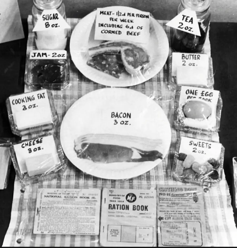 A black-and-white photo showing a weekly British World War II food ration: corned beef, bacon, cheese, cooking fat, sugar, tea, butter, jam, sweets, one egg, and a ration book, all labeled with their weights.
