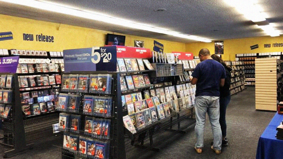 Two people browse DVDs in a brightly lit video rental store, with shelves full of movies and "new release" signs on the yellow walls.