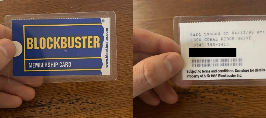 A hand holds a vintage Blockbuster membership card, showing the blue and yellow logo on the front. The back displays an issue date, address, phone number, and terms and conditions.