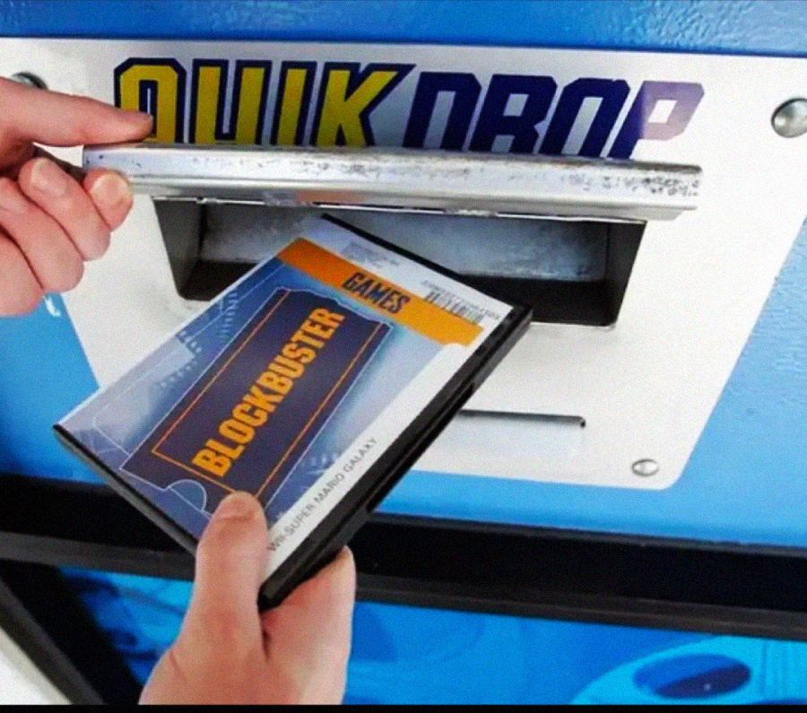 A person inserts a Blockbuster DVD case labeled "GALAXY" into a blue Quick Drop return slot on a Blockbuster video store kiosk.