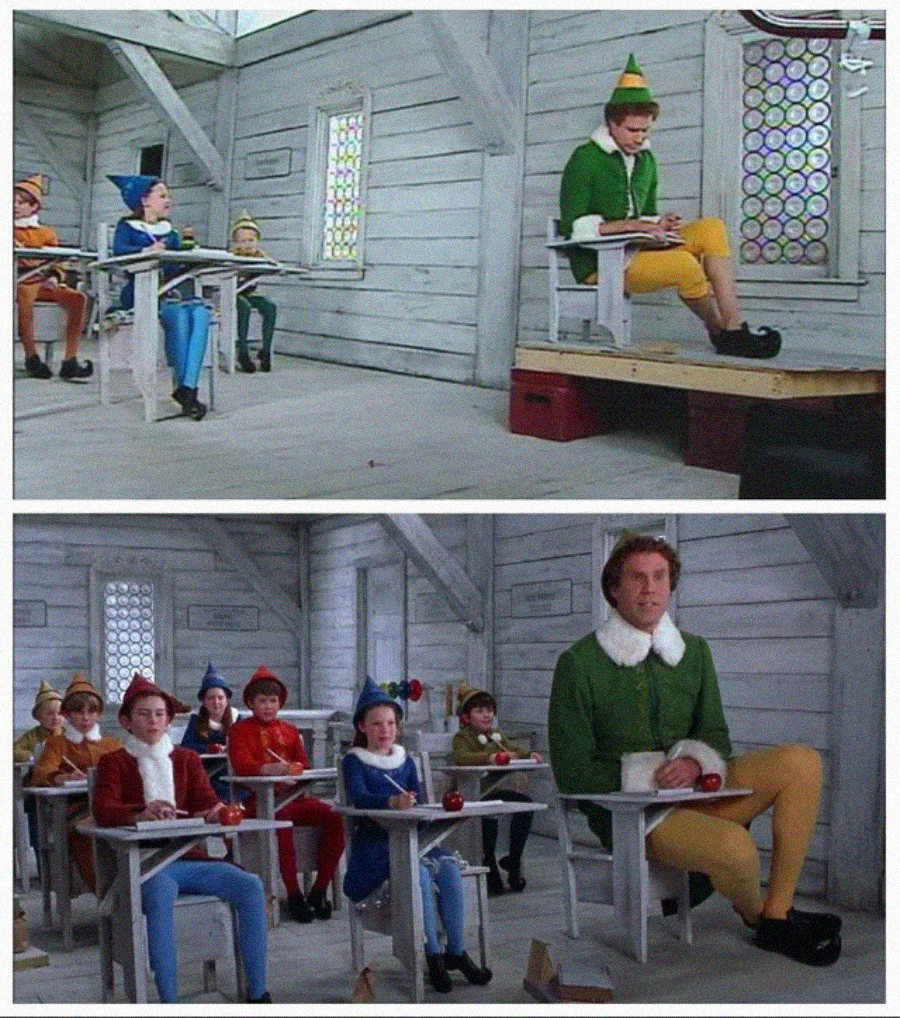 A man dressed as an elf sits much larger than the other elf children in a classroom, highlighting his size difference as he sits awkwardly at a small desk among them.