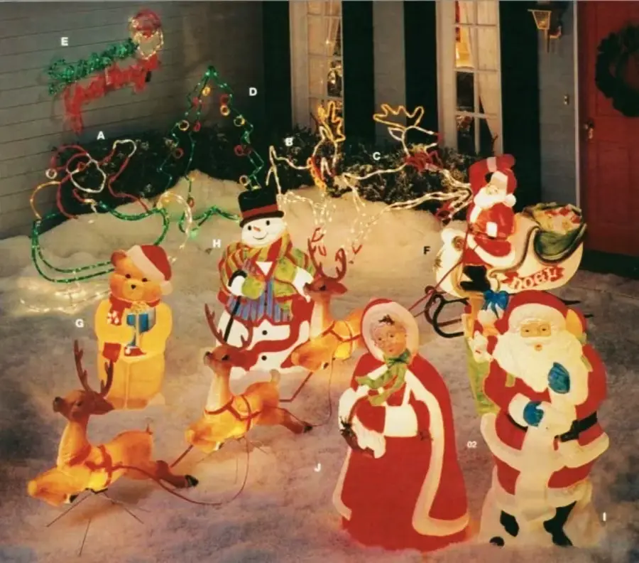 Colorful Christmas decorations in a snowy yard, featuring Santa Claus, Mrs. Claus, a snowman, reindeer, a teddy bear, a sleigh, and festive lights shaped like a wreath and other Christmas symbols.
