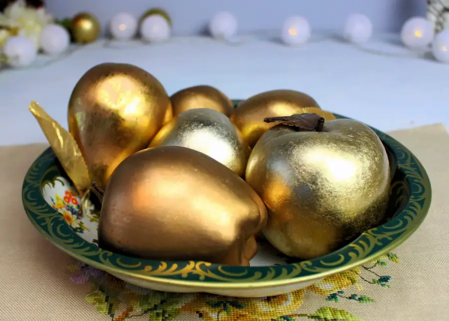 A decorative plate holds several shiny gold and bronze apples and pears, creating an elegant and festive display.