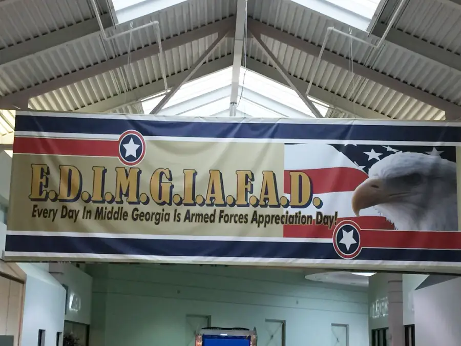 A banner reading "E.D.I.M.G.I.A.F.A.D. Every Day In Middle Georgia Is Armed Forces Appreciation Day" with a bald eagle, an American flag, and star symbols, hanging inside a building.