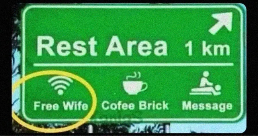 A green highway rest area sign reads "Rest Area 1 km" with icons for WiFi, coffee, and restrooms. The text humorously says "Free Wife" instead of "Free WiFi," and "Cofee Brick" instead of "Coffee Break.